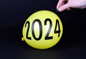 Hand uses a needle to burst a yellow balloon with 2024 text