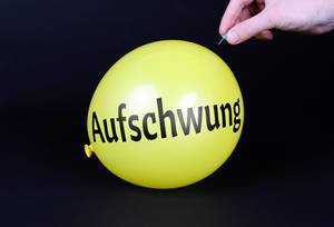 Hand uses a needle to burst a yellow balloon with Aufschwung text