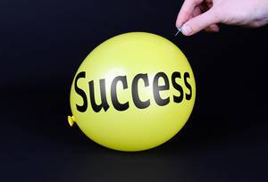 Hand uses a needle to burst a yellow balloon with Success text