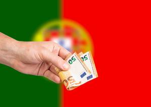 Hand with Euro banknotes over flag of Portugal