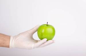 Hand with gloves holding green apple