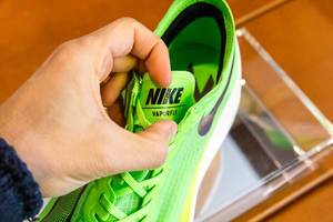 Hand zeigt Zunge mit Markennamen bei dem grünem Nike ZoomX Vaporfly NEXT% Laufschuh