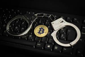 Handcuffs on computer keyboard with Bitcoin
