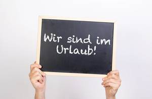 Hands holding blackboard with text Wir sing im Urlaub!