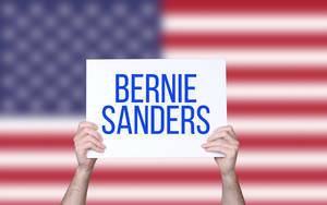 Hands holding board with Bernie Sanders text with USA flag background.jpg