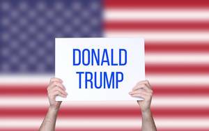 Hands holding board with Donald Trump text with USA flag background.jpg