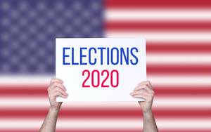 Hands holding board with Elections 2020 text with USA flag background
