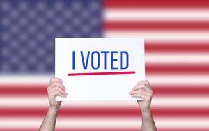 Hands holding board with I Voted text with USA flag background.jpg