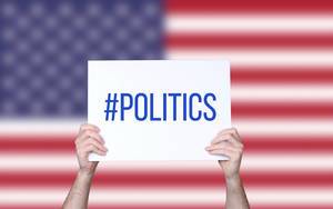 Hands holding board with #politics text with USA flag background