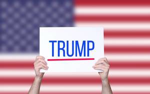 Hands holding board with Trump text with USA flag background