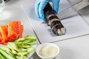 Hands in disposable gloves cutting sushi rolls on a cooking board (Flip 2019)