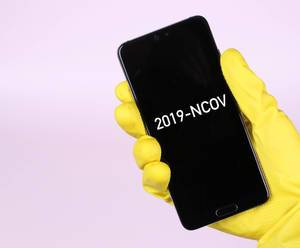 Hands in yellow rubber gloves holding mobile phone with 2019-NCOV text
