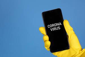 Hands in yellow rubber gloves holding mobile phone with Coronavirus text
