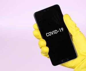 Hands in yellow rubber gloves holding mobile phone with Covid-19 text