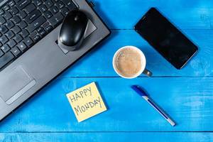 Happy Monday: Text auf Notizzettel wünscht einen guten Start in die Woche im Homeoffice, neben einem Laptop, Handy und Kaffeetasse