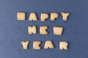 Happy new year aus Buchstabenkeksen vor schwarzem Hintergrund geschrieben - eine Nahaufnahme