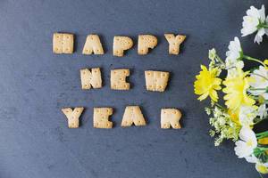 Happy new year aus Buchstabenkeksen vor schwarzem Hintergrund geschrieben