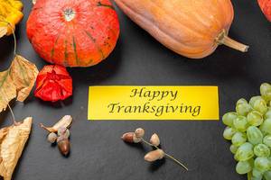 Happy thanksgiving wish on autumn background with pumpkins, grapes and dry leaves