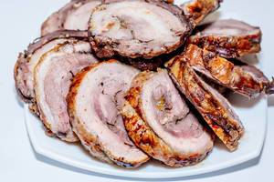 Hausgemachte, in Scheiben geschnittene Roulade aus Schweinefleisch mit Gewürzen auf weißem Teller