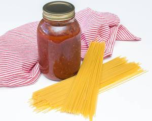 Hausgemachte Spaghettisoße mit ungekochten Spaghetti und rot-weißem Tuch