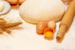 Hausgemachter Teig mit Wallholz und Zutaten wie Eier, Weizen und Mehl