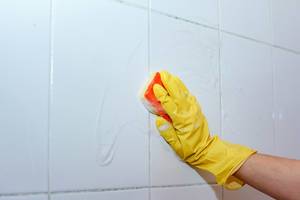 Hausmädchen reinigt die Badezimmer-Fliesen mit einem Schwamm und Latexhandschuhen