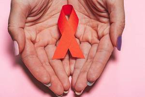 Healthcare, people, symbolic and medicine concept - close up of woman hands holding red AIDS awareness ribbon