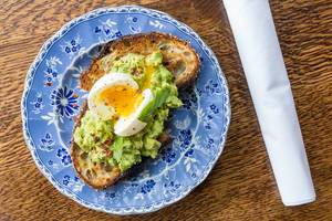 Healthy breakfast at the historic restaurant "The Allis" in Chicago: toast with avocado, egg, lime, chili and basil served on a blue plate in vintage style