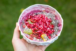 Healthy food: hand holds an acai bowl with Goji berries, pomegranate and chia seeds on green background