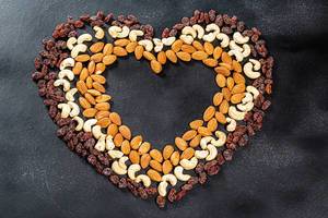 Heart lined from cashew nuts, almonds and raisins on a black background. Top view