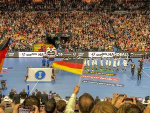 Helpers hold flag of the International Handball Federation on handball field in front of German team