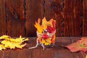 Herbstdekorationen  - Kerzenglas mit Laub und Eicheln geschmückt auf Holz-Hintergrund