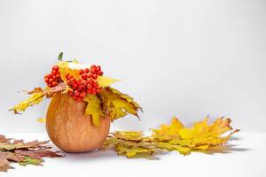 Herbstliches Arrangement - Ein Kürbis mit Kerze, roten Beeren und gelben Blättern auf weißem Hintergrund