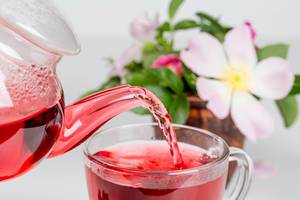 Hibiscus tea is poured from a teapot into a glass cup