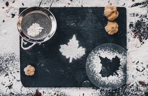 Hintergrund passend zum Kochen mit verstreutem Mehl in Blatt-Form auf einem schwarzen Küchentisch. Von oben fotografiert