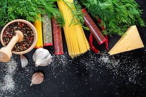 Hintergrundbild mit Kochzutaten und Konzeptbild zum Thema Ernährung, zeigt rohe Spaghetti, Knoblauch & Käse, zwischen Kräutern & Gewürzen