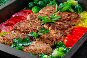 Homemade meat cutlets on a baking sheet with vegetables and herbs