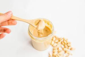 Homemade peanut butter in glass jar with hand and wooden spoon