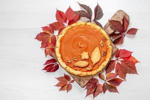 Homemade pumpkin pie with red autumn leaves on white wooden table. Top view (Flip 2019)