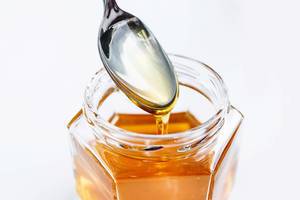 Honey in a glass jar with spoon on white background