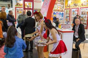 Hostessen in rot-schwarzem Kleid bieten Kindern Süßigkeiten an bei der Anuga Lebensmittelmesse in Köln