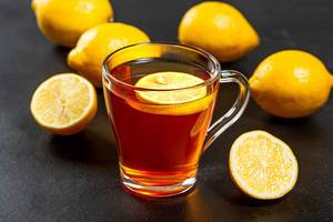 Hot tea with fresh yellow lemons on black background
