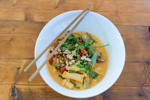 Hot, vegan organic Tofu Pho-sot cari in red coconut curry from Chum Chay Restaurant, with bush beans, oyster mushrooms & cashew nuts on a wooden table
