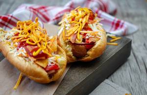 Hotdogs mit knusprigem Speck, geriebenem Käse, Chips, Cherrytomaten und Zwiebel