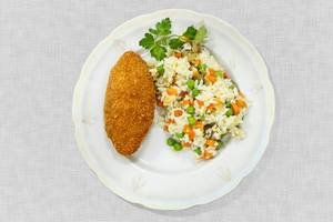 Hühnerfleischgericht "Kiewer Kotelett" mit Gemüsereis auf weißem Teller