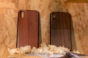 Hüllen für Smartphones aus Holz mit Infobroschüre vor Spanplatte und Sägespänen