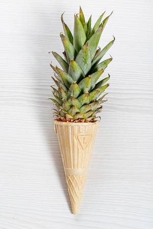 Ice cream cone with pineapple leaves on white background. Fruit and candy concept