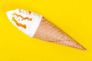 Ice cream in sweet waffle cone with caramel topping in yellow background