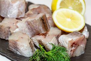 In mundgerechte Stücke geschnittener frischer roher Fisch mit Zitrone und Kräutern auf Schieferplatte