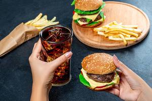 In one hand Burger, in the second the glass with cold Cola. The concept of unhealthy eating (Flip 2019)